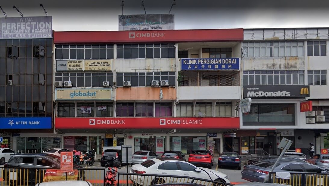 Pemandangan aras jalan luar bangunan komersial bertingkat yang menampilkan: Tingkat Bawah: Sebuah kedai cawangan CIMB Bank dan CIMB Islamic. Tingkat Atas: Papan tanda untuk Klinik Pergigian Dorai, Global Art dan agensi insurans. Persekitaran: Di sebelah kanan ialah McDonald's, dan di hujung kiri ialah Affin Bank