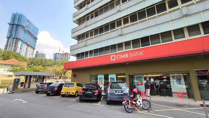Pemandangan aras jalan luar cawangan CIMB Bank Jalan Duta yang memaparkan papan tanda merah besar di atas pintu masuk, dengan beberapa kereta yang diletakkan di latar depan dan bangunan tinggi di latar belakang