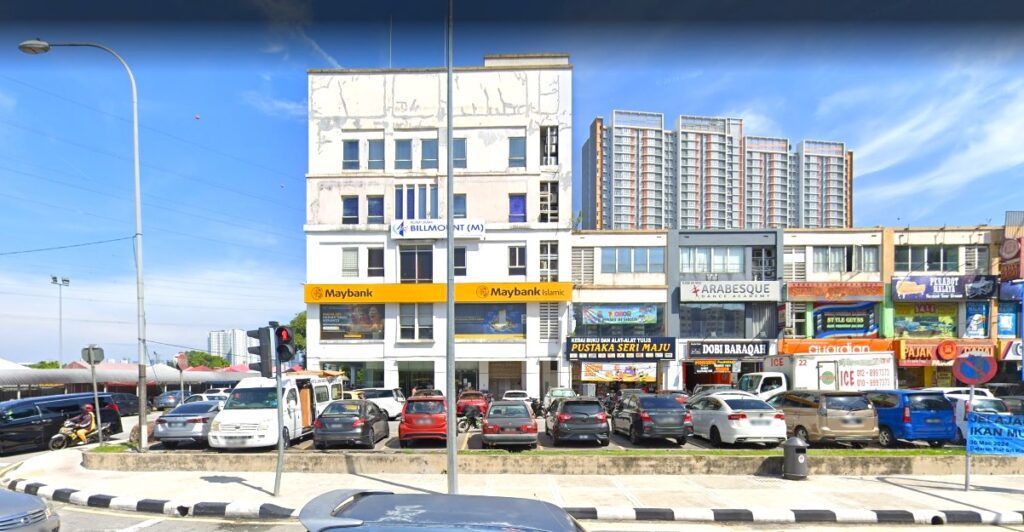 Pemandangan aras jalan siang hari barisan komersial di Bandar Sri Permaisuri. Titik tumpuan ialah cawangan Maybank dan Maybank Islamic berwarna kuning yang menonjol di tingkat bawah. Di kanan, perniagaan bersebelahan termasuk Pustaka Seri Maju, Akademi Tarian Arabesque, Dobi Baraqah, dan farmasi Guardian