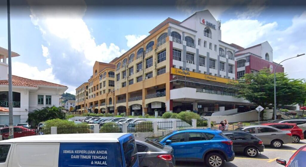 Pemandangan luar bangunan komersial bertingkat di Taman Setiawangsa, yang menampilkan cawangan Maybank di tingkat bawah. Bangunan itu berwarna putih dan kuning dengan tingkap melengkung, terletak di belakang tempat letak kereta yang sibuk dipenuhi dengan pelbagai jenis kereta