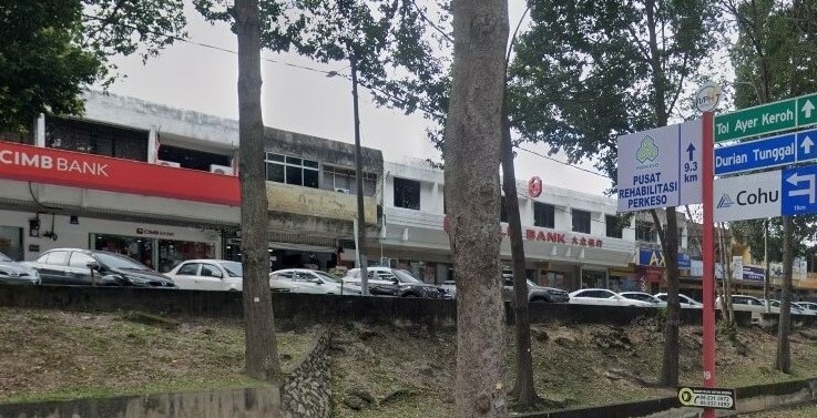 Gambar luaran cawangan CIMB Bank di Ayer Keroh, Melaka. Bank itu terletak di sebuah bangunan komersial dua tingkat berwarna putih yang sebahagiannya dikaburkan oleh pokok-pokok tinggi di latar depan. Di kanan, papan tanda jalan berbilang arah menghala ke Tol Ayer Keroh, Durian Tunggal, dan Cohu, bersebelahan dengan papan tanda Pusat Rehabilitasi PERKESO