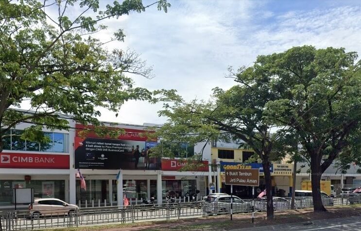 Pemandangan aras jalan cawangan CIMB Bank di Malaysia, yang terletak di deretan bangunan komersial dua tingkat berwarna putih. Jenama CIMB merah dan putih yang besar kelihatan di bahagian hadapan kedai, di samping papan tanda jalan berarah coklat yang menghala ke Bukit Tambun dan Jeti Pulau Aman