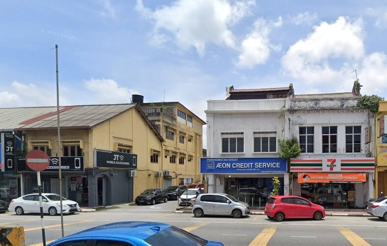 Gambar tepi jalan menunjukkan deretan rumah kedai lama di Banting, Malaysia. Bangunan utama ialah bangunan putih dua tingkat dengan perkataan dan logo "AEON CREDIT SERVICE", diapit kedai 7-Eleven di sebelah kanan dan bangunan kuning dengan papan tanda "JT MOBILE ACCESSORIES" di sebelah kiri