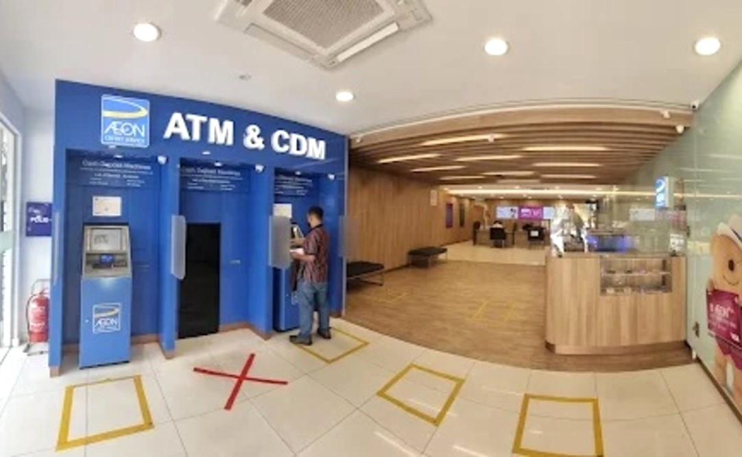 Bahagian dalam cawangan AEON Credit Ipoh, menunjukkan kawasan ATM & CDM (Mesin Deposit Tunai), dengan pelanggan menggunakan salah satu mesin. Selebihnya bilik mempunyai panel kayu nipis di dinding dan siling, lantai berjubin dengan penanda jarak sosial kuning, dan ruang menunggu tambahan boleh dilihat di latar belakang