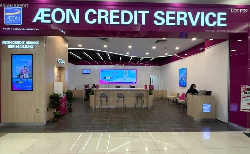 Gambar dalaman moden cawangan AEON Credit Services di Seri Manjung, menampilkan skema warna magenta dan putih, kaunter perkhidmatan pusat dengan bangku, skrin paparan digital yang memaparkan promosi dan seorang kakitangan yang bekerja di meja sisi