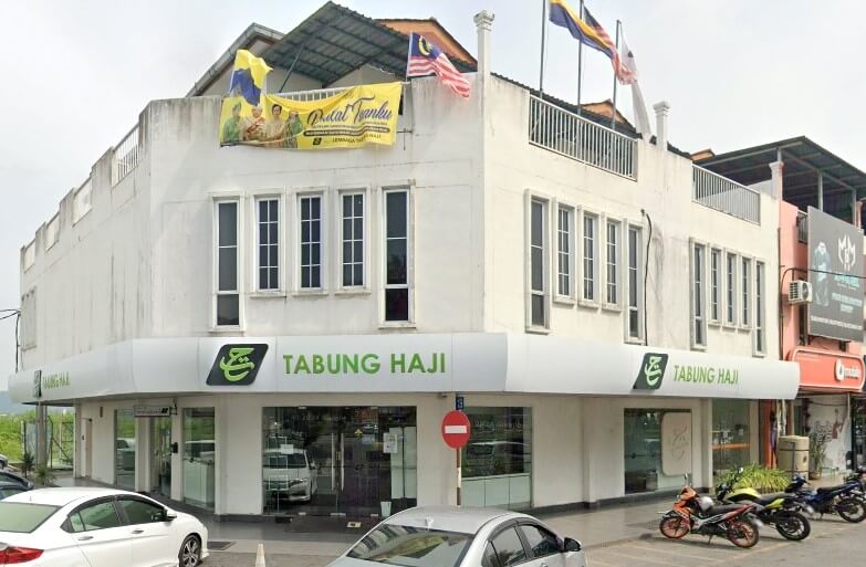 Pemandangan luar bangunan Tabung Haji dua tingkat berwarna putih di sudut jalan, menampilkan papan tanda hijau dan putih, tingkap kaca, dan bendera Malaysia di atas bumbung
