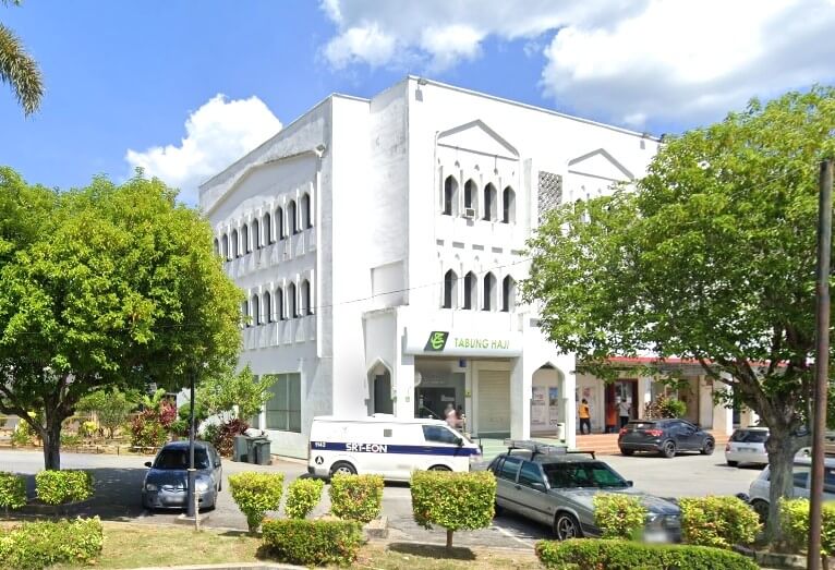 Sebuah bangunan putih tiga tingkat dengan tingkap melengkung ala Islam, dengan papan tanda "Tabung Haji" berwarna hijau di atas pintu masuk. Sebuah van keselamatan putih dan beberapa buah kereta diletakkan di tempat letak kereta di hadapan, dikelilingi oleh pokok-pokok hijau dan pagar tanaman yang terurus rapi