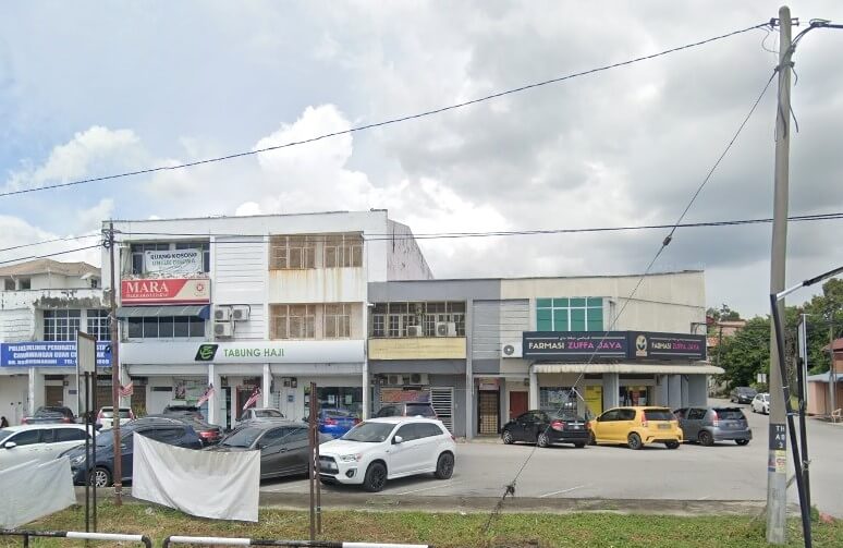 Pemandangan jalan luar blok bangunan komersial di Guar Chempedak, Malaysia, termasuk pejabat Tabung Haji, pejabat MARA, dan Farmasi Zuffa Jaya, dengan beberapa kereta diletakkan di hadapan