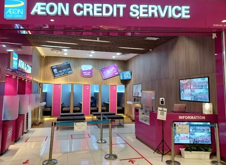 Interior AEON Credit AEON Mall Nilai. Pintu masuk mempunyai papan tanda bercahaya terang yang berbunyi "AEON CREDIT SERVICE" dalam teks putih pada latar belakang merah jambu