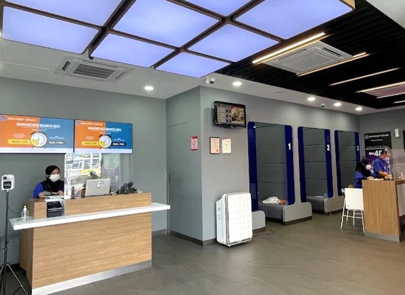 Di dalam pejabat AEON Credit Melaka, menunjukkan kaunter perkhidmatan pelanggan di sebelah kiri, di mana seorang pekerja wanita bertopeng duduk di belakang partition lutsinar dan komputer