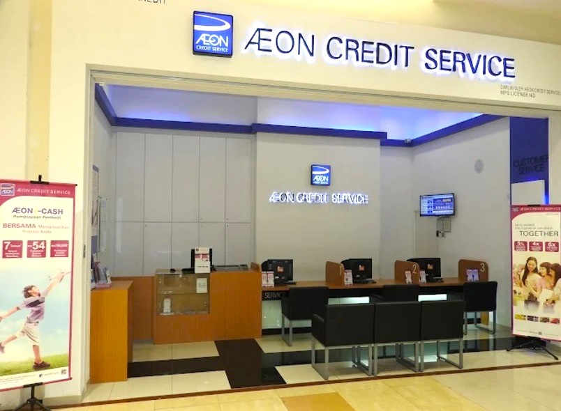 Foto bahagian dalam dan kotak paparan pejabat AEON Credit Seremban 2, menunjukkan kaunter dengan dua meja wakil perkhidmatan, papan tanda bercahaya terang dan sepanduk promosi di kedua-dua belah pihak