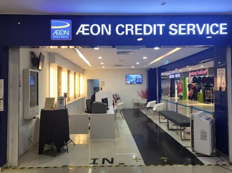 Bahagian dalam cawangan AEON Credit Wangsa Maju, menampilkan meja penyambut tetamu yang terang benderang, kerusi putih, bangku hitam untuk menunggu dan skrin paparan di dinding belakang