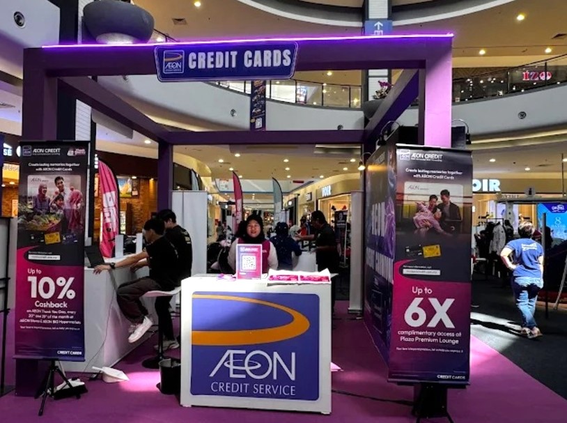 Gerai promosi untuk AEON Credit Service yang menampilkan bangunan berwarna ungu dengan papan tanda "CREDIT CARDS", terletak di pusat membeli-belah, AEON Credit Bandaraya Melaka