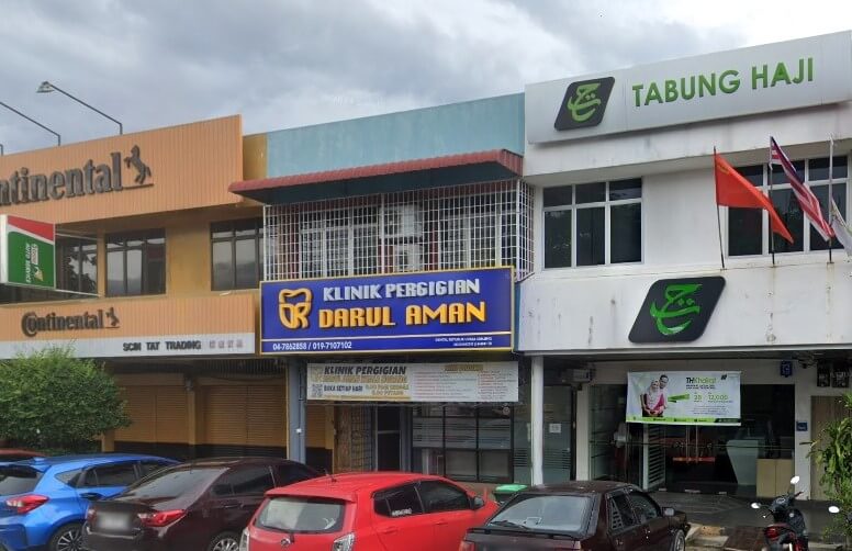 iga rumah kedai bersebelahan dengan kereta diletakkan di hadapannya: Continental SCIN TAT TRADING (bangunan oren, kiri), Klinik Pergigian Darul Aman (papan tanda biru, tengah), dan Tabung Haji (bangunan putih, kanan)