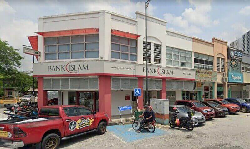 Pandangan luar cawangan Bank Islam dua tingkat di sudut jalan di Ampang, Malaysia, menampilkan penjenamaan putih dan merah, dengan kereta dan motosikal yang diletakkan di hadapan