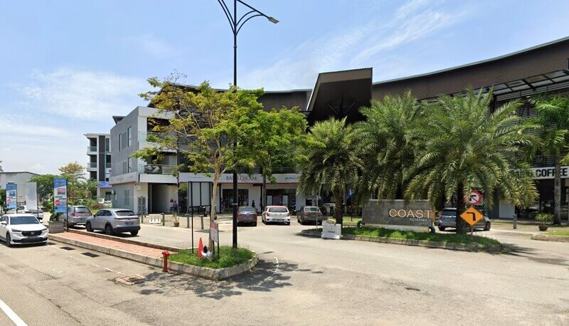 Pemandangan aras jalan luar Bank Islam Malaysia Berhad di Chukai, Terengganu, terletak di dalam kompleks komersial Pantai Kemaman moden. Imej itu menunjukkan kedai bank dan papan tanda "Coast Coast Kemaman", dengan beberapa kereta yang diletakkan dan pokok-pokok tropika berbaris di pintu masuk berturap