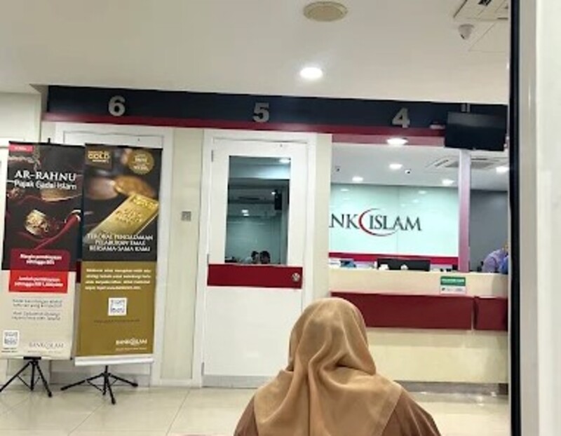 Gambar dalaman cawangan Bank Islam di Malaysia. Seorang yang memakai tudung coklat duduk di latar depan, menghadap kaunter perkhidmatan bernombor 4, 5, dan 6