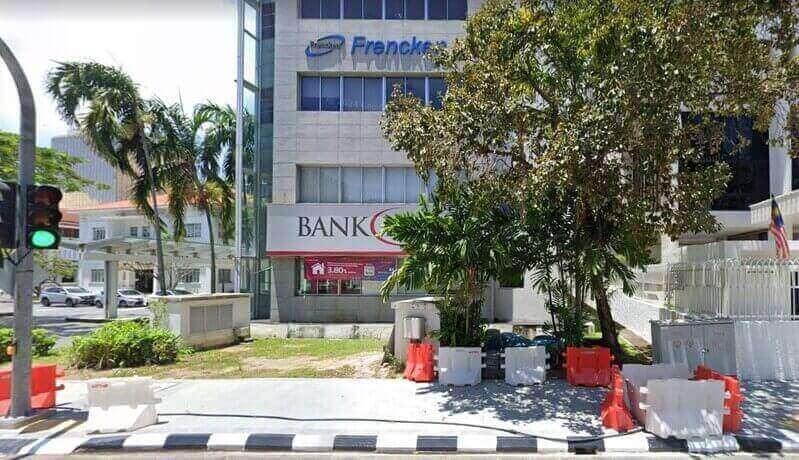 Pandangan luar cawangan Bank Islam George Town yang terletak di bangunan komersial bertingkat dengan papan tanda Frencken Group, yang menampilkan pintu masuk aras jalan, sepanduk promosi merah dan bendera Malaysia