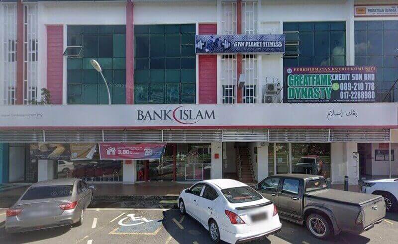Pemandangan luar cawangan Bank Islam Sandakan di Sabah, Malaysia, yang terletak di bangunan komersial bertingkat yang menampilkan kedai putih dan merah dengan perniagaan berdekatan seperti Gym Planet Fitness dan Greatfame Dynasty Credit
