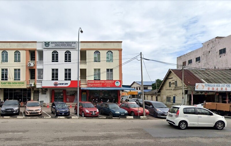 Pemandangan aras jalan bangunan komersial bertingkat di Mersing, Malaysia, yang menampilkan pejabat KWSP (EPF) dengan jenama merah dan putihnya yang tersendiri. Bangunan ini juga menempatkan "Kedai Gunting Rambut Purnama" dan pejabat RISDA. Beberapa buah kereta diletakkan di hadapan kedai-kedai, dengan struktur kayu lama kelihatan di sebelah kanan