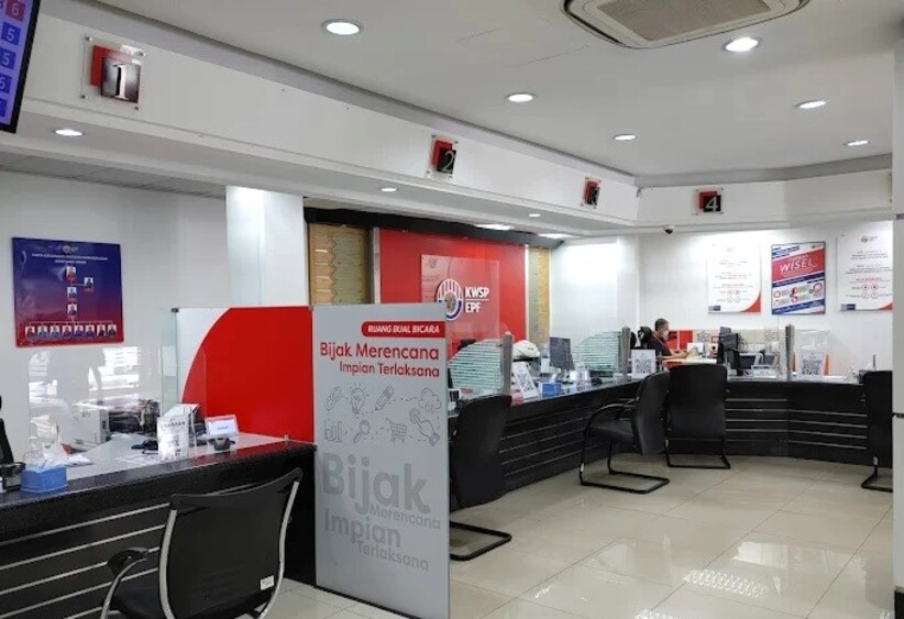 Bahagian dalam pejabat Kumpulan Wang Simpanan Pekerja (KWSP/EPF) di Malaysia, menampilkan beberapa kaunter perkhidmatan bernombor 1 hingga 4 di bawah soffit putih. Sekatan merah dan putih di latar depan memaparkan slogan "Bijak Merencana Impian Terlaksana." Pejabat ini bersih dan terang benderang, dengan poster di dinding dan seorang kakitangan duduk di salah satu kaunter