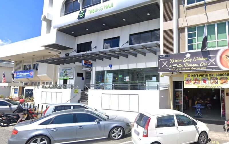 Pandangan luar bangunan bertingkat putih yang menampilkan cawangan Tabung Haji dengan papan tanda hijau, terletak di sebelah sebuah restoran bernama Kafe Patin Ori Bangau