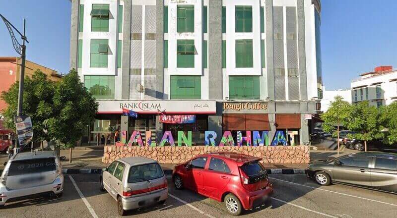Pemandangan aras jalan Bank Islam dan Kopi Rengit yang terletak di Jalan Rahmat di Batu Pahat, menampilkan papan tanda "JALAN RAHMAT" berwarna-warni dan meletakkan kereta di latar depan