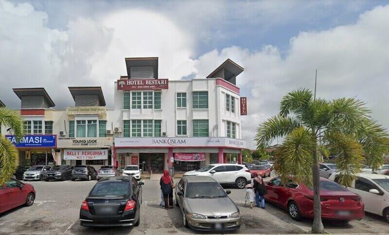 Pemandangan aras jalan cawangan Bank Islam yang terletak di tingkat bawah bangunan bertingkat putih di Jasin, Malaysia, dengan Hotel Bestari terletak di atasnya dan pelbagai kereta diletakkan di hadapan