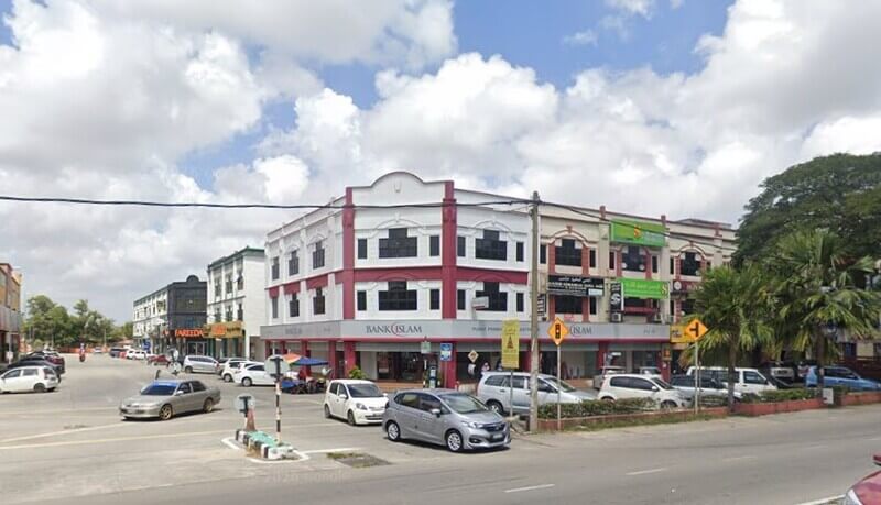 Pemandangan aras jalan cawangan Bank Islam Malaysia Berhad di Kubang Kerian, menampilkan perincian seni bina putih dan merah, dengan beberapa kereta yang diletakkan dan langit cerah di latar belakang