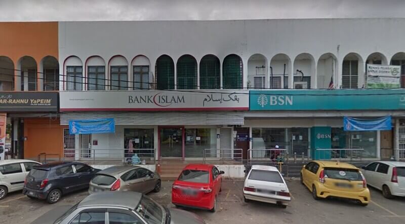 Pandangan hadapan cawangan Bank Islam Malaysia Berhad Machang dan cawangan BSN yang terletak bersebelahan dalam deretan lot kedai dua tingkat berwarna putih dengan tingkap melengkung. Beberapa buah kereta diletakkan di lot di hadapan bangunan