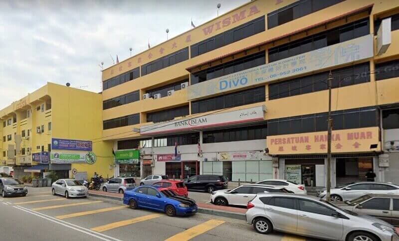 Pemandangan luar cawangan Bank Islam Malaysia Berhad di Muar, terletak di tingkat bawah bangunan komersial bertingkat berwarna kuning (Wisma Persatuan Hakka Muar) dengan kereta-kereta diletakkan di sepanjang jalan di hadapan