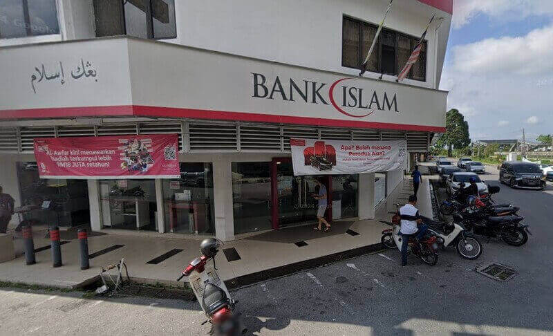 Pandangan luar cawangan pejabat Bank Islam Malaysia Berhad Parit Buntar yang menampilkan papan tanda kedai merah putih, sepanduk promosi dan tempat letak kereta di tepi jalan