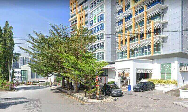 Pemandangan aras jalan cawangan Bank Islam Malaysia Berhad di Seremban, menampilkan bangunan bertingkat moden dengan aksen putih dan oren, dinaungi oleh pokok-pokok hijau