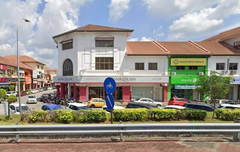 Pandangan luar bangunan sudut bertingkat putih yang menempatkan cawangan Bank Islam Malaysia Berhad di Sungai Petani, Malaysia, yang terletak bersebelahan dengan kedai Maxis hijau di sepanjang jalan yang sibuk dengan kereta dan motosikal yang diletakkan.