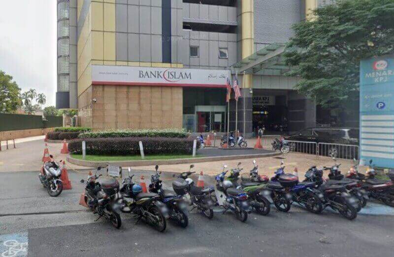 Pandangan luar cawangan Bank Islam yang terletak di kaki bangunan bertingkat moden, dengan beberapa motosikal diletakkan di latar depan dan papan tanda Menara KPJ kelihatan di sebelah kanan