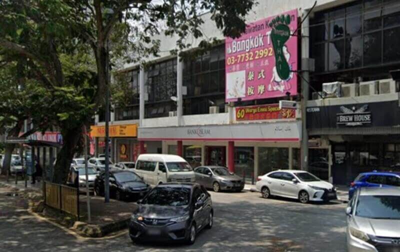 Pemandangan aras jalan cawangan Bank Islam di Taman Tun Dr Ismail, menampilkan papan tanda putih dengan aksen merah. Bank ini terletak di barisan komersial bersebelahan dengan perniagaan seperti The Brew House dan Bangkok Thai Massage, dengan beberapa kereta diletakkan di sepanjang jalan