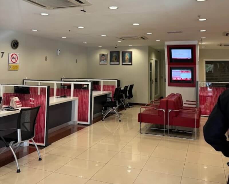 Pemandangan dalaman cawangan Bank Islam Malaysia Berhad di Universiti Malaya, menampilkan kaunter perkhidmatan moden dengan pembahagi bercorak merah, kerusi hitam ergonomik dan ruang menunggu kulit merah. Pejabat yang bersih dan terang ini menampilkan skrin paparan digital dan potret orang kenamaan Malaysia di dinding belakang